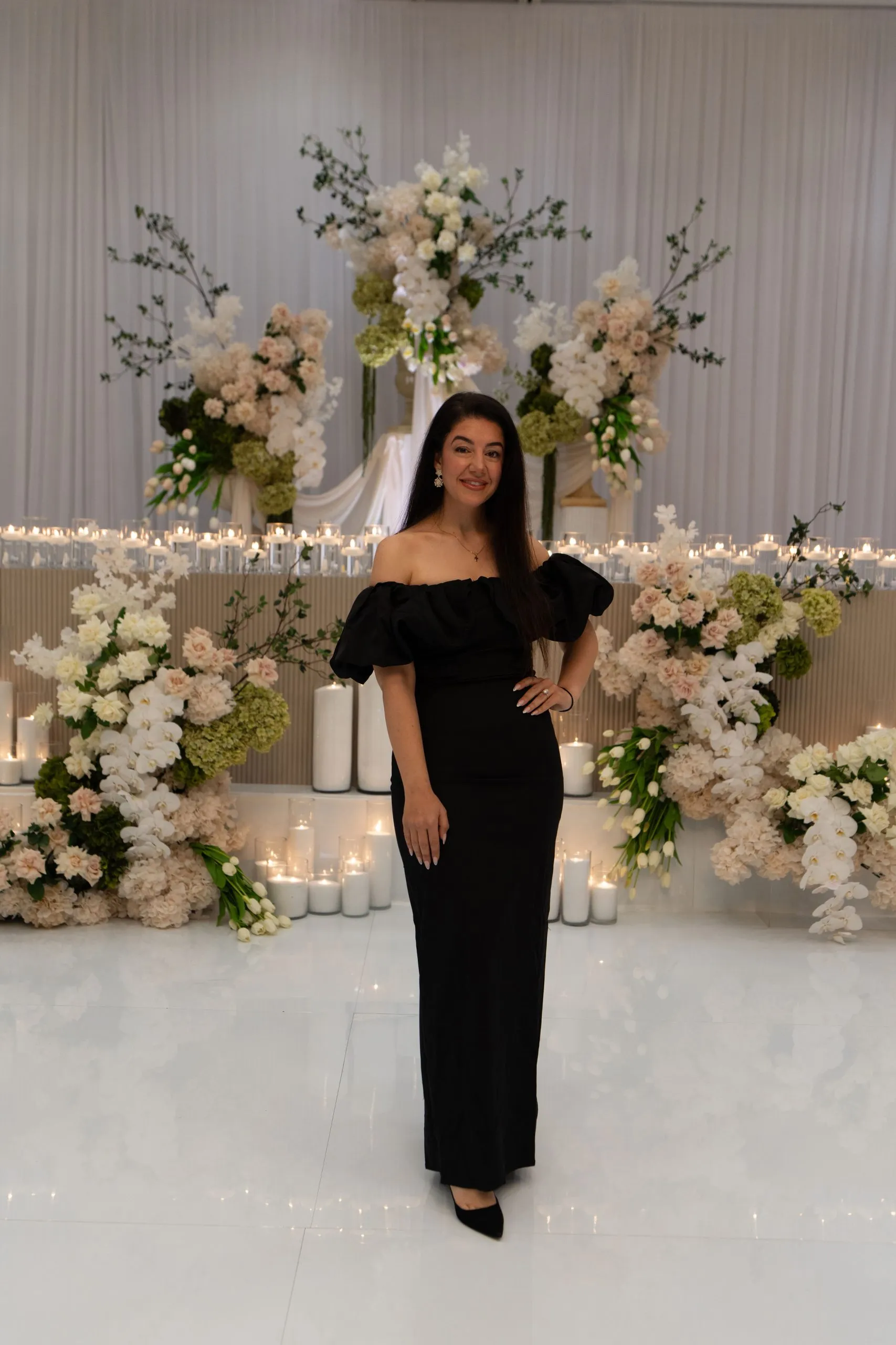 Demetra, founder and lead stylist at LLS Events and Hire, in front of a white floral and candle installation at a Sydney wedding